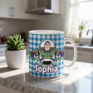 May include: A white ceramic mug featuring a blue and white gingham pattern background. The mug displays a graphic of the character Buzz Lightyear with the name Sophia printed in purple script lettering below the character on the front surface.