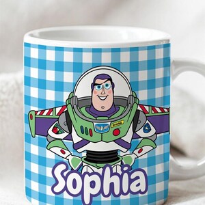 May include: A white ceramic mug featuring a blue and white checkered pattern background. The center displays a colorful illustration of the character Buzz Lightyear in his space suit. Below the character, the name Sophia is printed in purple text.