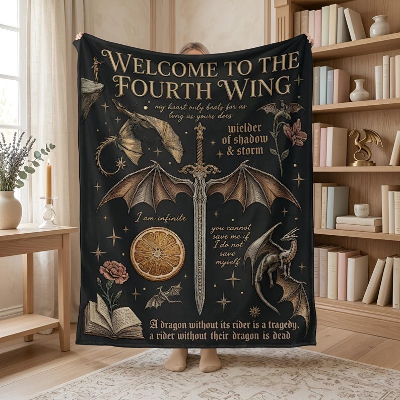 Puede incluir: Manta negra con tem&aacute;tica de fantas&iacute;a, con una espada con alas de drag&oacute;n, dragones y elementos florales. El texto incluye "Welcome to the Fourth Wing" y otras frases. La manta est&aacute; sujeta por una persona.