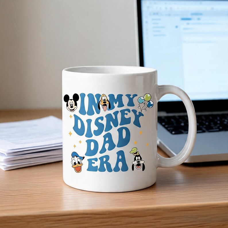 Puede incluir: Una taza de cer&aacute;mica blanca con texto azul que dice IN MY DISNEY DAD ERA. El dise&ntilde;o incluye peque&ntilde;as ilustraciones coloridas de Mickey Mouse, Goofy, el Pato Donald y un grupo de globos, acentuado por diminutas estrellas amarillas dispersas.