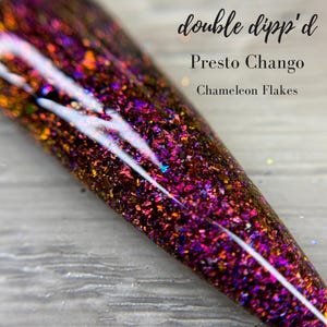 May include: A close-up of a nail with a vibrant, multi-colored design. The nail is covered in iridescent chameleon flakes, with shades of purple, orange, and gold. The text "double dipp'd", "Presto Chango", and "Chameleon Flakes" are visible.