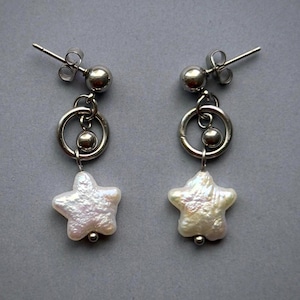 May include: A pair of drop earrings featuring a silver-toned metal post with a small sphere, a circular ring, and a dangling white iridescent star-shaped pearl. The earrings include standard metal butterfly backs for secure attachment to the earlobe.