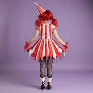 May include: A red and white striped costume with a matching hat. The dress has a flared skirt with jagged edges, paired with black fishnet stockings and white boots with black accents. The costume is set against a purple background.