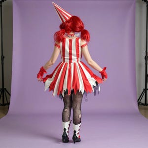 May include: A red and white striped circus-themed costume. The outfit includes a matching hat, dress, and gloves. The dress has a flared skirt with jagged edges. The model is wearing black fishnet stockings and white boots with black heels.