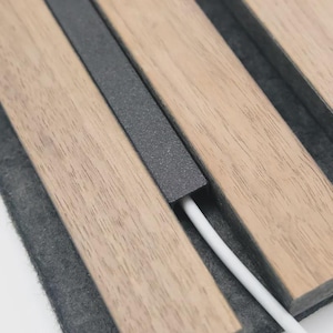 Puede incluir: Primer plano de un organizador de escritorio de madera con una tira de metal gris oscuro y un cable blanco. El organizador tiene un acabado de madera marrón claro y una base de fieltro gris oscuro. El cable está insertado en una ranura.