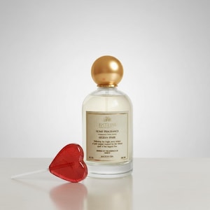 Può includere: Un flacone di profumo per la casa in vetro trasparente con tappo e etichetta dorati, accanto a un lecca-lecca rosso a forma di cuore. L'etichetta recita "FXTEINI HOME FRAGRANCE AEGEAN SPARK". Il lecca-lecca è su un bastoncino bianco.