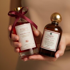 Könnte beinhalten: Zwei Glasflaschen mit Duftstoffen werden in den Händen einer Person gehalten. Die Flasche links ist mit einer roten Flüssigkeit gefüllt und hat ein weinrotes Band. Auf dem Etikett steht "AEGEAN RUBY GLOW". Die Flasche rechts ist braun mit einem goldenen Verschluss und trägt die Aufschrift "KARYDAKI DELIGHT".