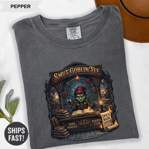 Może przedstawiać: Szara koszulka Comfort Colors z nadrukiem "Smut Goblin Tee". Grafika przedstawia zielonego goblina czytającego książkę, z napisami "Dark Romance", "Readers Club" i "Spicy Book Lover".