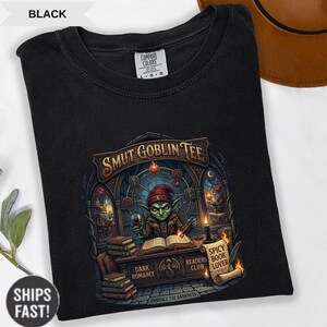 Może przedstawiać: Czarny t-shirt z grafiką przedstawiającą zielonego goblina w czerwonej czapce, trzymającego kieliszek wina i czytającego. Tekst "SMUT GOBLIN TEE" znajduje się nad goblinem. Dodatkowy tekst to "DARK ROMANCE", "READERS CLUB" i "SPICY BOOK LOVER".