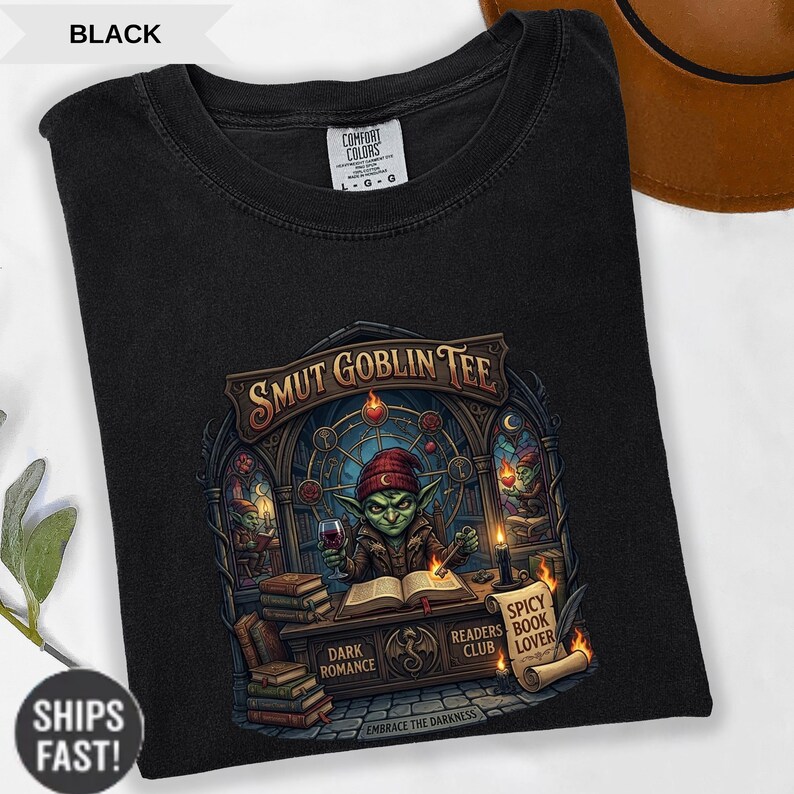 Może przedstawiać: Czarny t-shirt z grafiką przedstawiającą zielonego goblina w czerwonej czapce, trzymającego kieliszek wina i czytającego. Tekst "SMUT GOBLIN TEE" znajduje się nad goblinem. Dodatkowy tekst to "DARK ROMANCE", "READERS CLUB" i "SPICY BOOK LOVER".