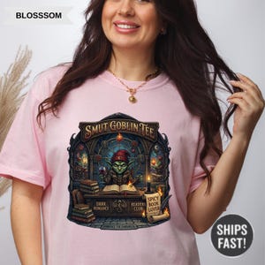 Może przedstawiać: Jasnor&oacute;żowa koszulka z napisem "SMUT GOBLIN TEE" i grafiką goblina czytającego książkę. Grafika zawiera słowa "DARK ROMANCE", "SPICY READERS BOOK CLUB LOVER" i "EMBRACE THE DARKNESS".