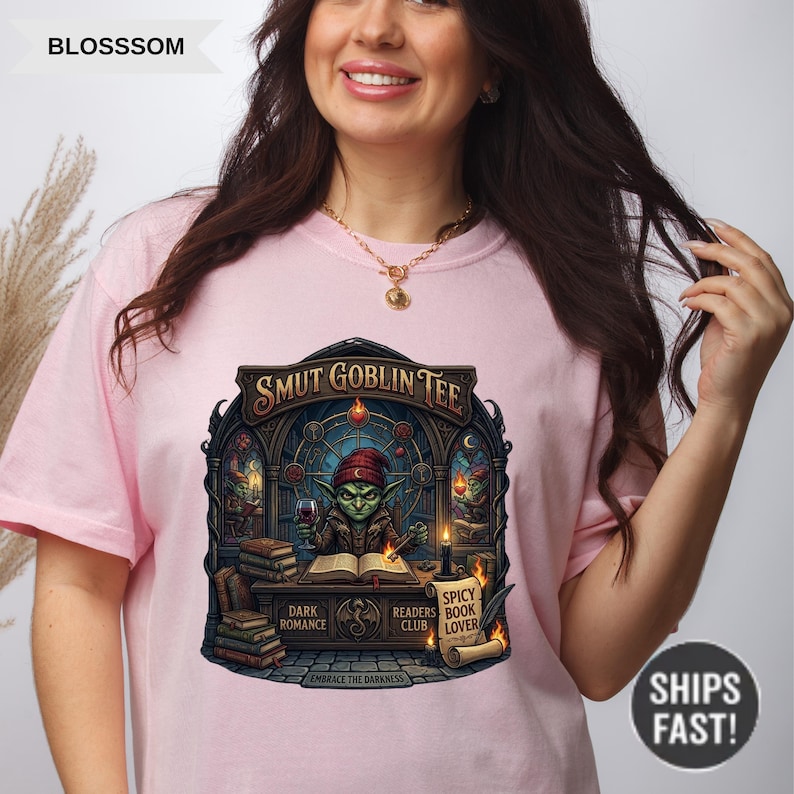 Może przedstawiać: Jasnor&oacute;żowa koszulka z napisem "SMUT GOBLIN TEE" i grafiką goblina czytającego książkę. Grafika zawiera słowa "DARK ROMANCE", "SPICY READERS BOOK CLUB LOVER" i "EMBRACE THE DARKNESS".