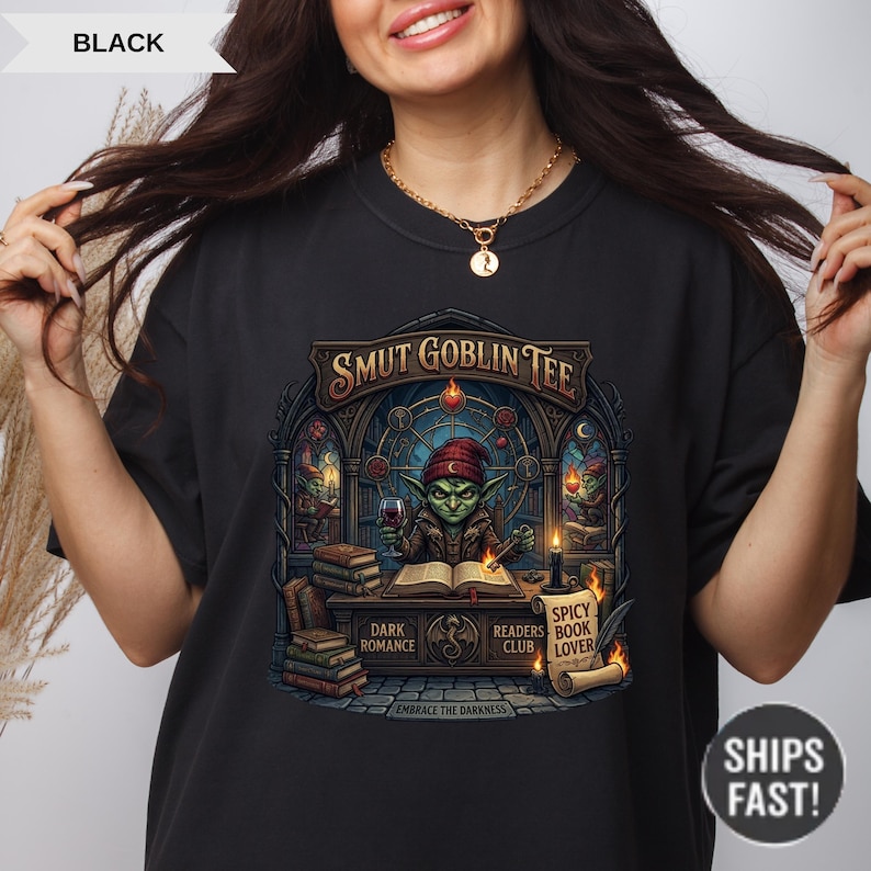 Może przedstawiać: Czarny t-shirt z grafiką przedstawiającą zielonego goblina czytającego książkę, trzymającego kieliszek wina, oraz napisem "SMUT GOBLIN TEE". Dodatkowy tekst zawiera "DARK ROMANCE", "READERS CLUB" i "SPICY BOOK LOVER".