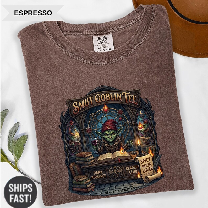 Może przedstawiać: Koszulka w kolorze espresso z grafiką z napisem "SMUT GOBLIN TEE". Projekt przedstawia zielonego goblina trzymającego kieliszek wina, z książkami i świecami. Koszulka wykonana jest z materiału Comfort Colors.