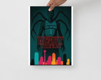 May include: A poster featuring a basketball player in a San Antonio jersey with the number 1. The poster has a dark teal background with the text "WEMBY THINGS" in red, and a city skyline silhouette at the bottom.
