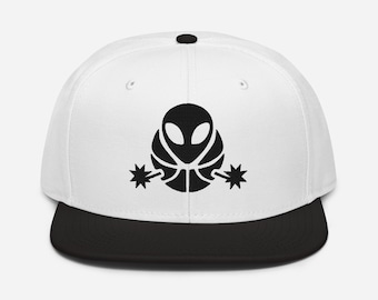 May include: A white snapback cap with a black brim and a black button on top. The front panel features a black graphic of an alien head centered above two small star-shaped icons extending outward on each side of the alien figure.