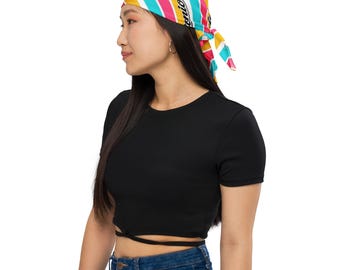 May include: A colorful bandana with vertical stripes in yellow, turquoise, pink, and white. The bandana has a logo on the side and is tied at the back. The person is wearing a black crop top and blue jeans.