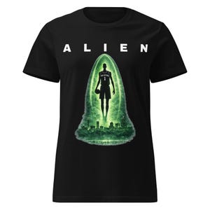 Könnte beinhalten: Schwarzes T-Shirt mit dem Wort "ALIEN" in weißen Großbuchstaben. Darunter befindet sich eine grüne Grafik eines Basketballspielers in einem leuchtenden Oval, mit einer Skyline am unteren Rand.