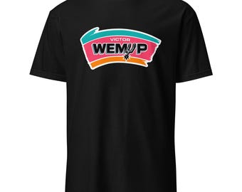 May include: Black t-shirt featuring a colorful graphic with the text "VICTOR WEM★P". The graphic includes teal, pink, and orange brushstrokes, and a star. The shirt is made of a soft material.