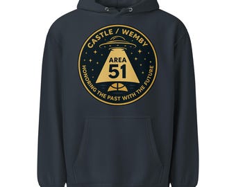 May include: Navy blue hooded sweatshirt with a circular graphic. The graphic features a gold UFO, the text "CASTLE / WEMBY" and "AREA 51". The text "HONORING THE PAST WITH THE FUTURE" is also included. The sweatshirt has a front pocket.