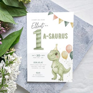 Puede incluir: Una invitación de cumpleaños con temática de dinosaurios. La invitación presenta un dinosaurio de dibujos animados, globos y el texto "Elliot es un A-SAURUS". La invitación incluye la fecha, hora y lugar de la fiesta.