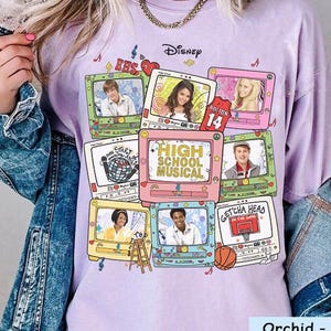Può includere: T-shirt color orchidea con una grafica di televisori retrò che mostrano personaggi e la scritta "High School Musical". Il design include il logo Disney e la scritta "Get'cha Head". La maglietta è una maglietta comfort color.