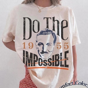 Pu&ograve; includere: T-shirt color avorio con la scritta "Do The Impossible" e un ritratto vintage. I numeri "1955" sono stampati sulla maglietta. La maglietta &egrave; abbinata a pantaloncini a scacchi rossi e bianchi.