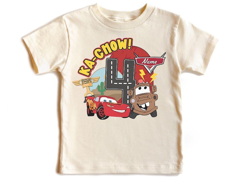 May include: Cream-colored t-shirt featuring a graphic of Lightning McQueen and Mater from the movie Cars. The design includes the text "Ka-Chow!" and a large number "4", with space for a name. A fun birthday shirt.