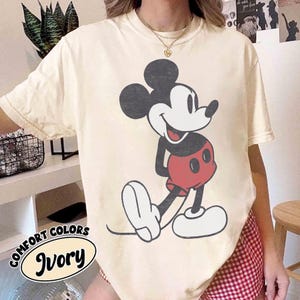 Peut inclure: T-shirt ivoire Comfort Colors avec un dessin de Mickey Mouse. Le personnage de dessin anim&eacute; est en noir, rouge et blanc. Le t-shirt a une coupe d&eacute;contract&eacute;e et les mots "Comfort Colors" et "Ivory" sont imprim&eacute;s en bas &agrave; gauche.