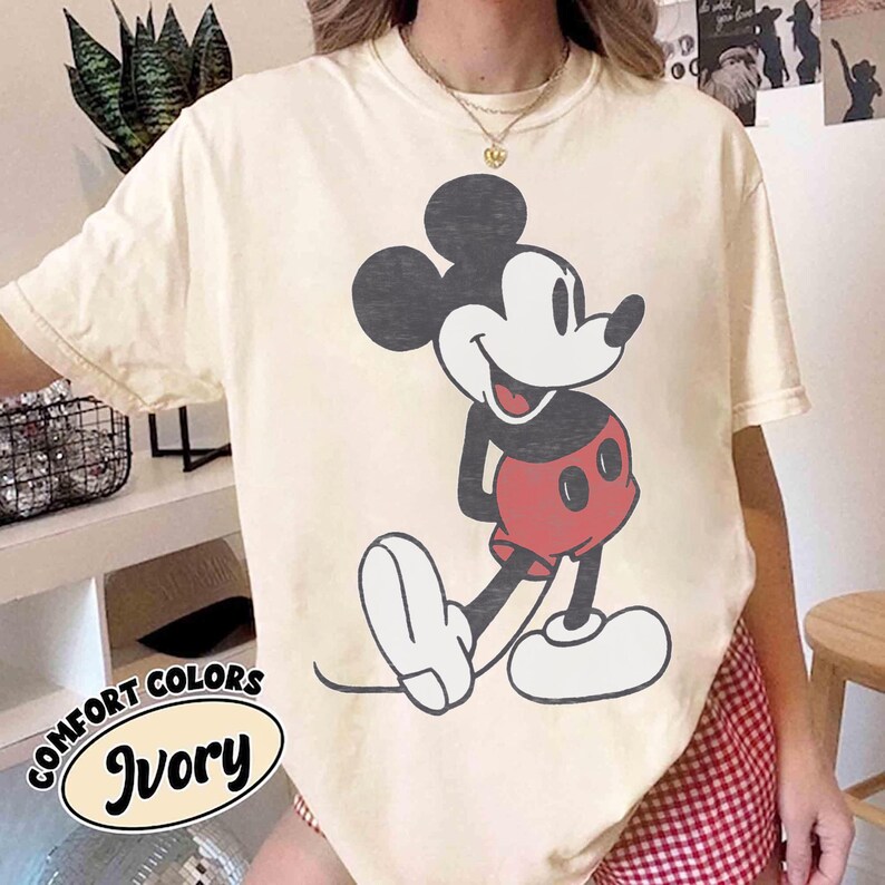 Peut inclure: T-shirt ivoire Comfort Colors avec un dessin de Mickey Mouse. Le personnage de dessin anim&eacute; est en noir, rouge et blanc. Le t-shirt a une coupe d&eacute;contract&eacute;e et les mots "Comfort Colors" et "Ivory" sont imprim&eacute;s en bas &agrave; gauche.