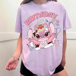 K&ouml;nnte beinhalten: Helllila T-Shirt mit einem Cartoon-Charakter und dem Text "BIRTHDAY Girl". Der rosa Charakter hat gro&szlig;e Augen und ein Dessert auf dem Kopf. Feuerwerk und Partydekorationen sind ebenfalls zu sehen.