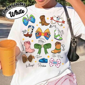 May include: White t-shirt featuring cartoon bow and boot designs with character names like Woody, Buzz Lightyear, and Bo Peep. The shirt includes the text "COMFORT COLORS" and "White" in a circular design.
