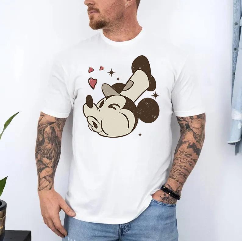 May include: White t-shirt featuring a vintage-style illustration of a cartoon mouse with a wink, hearts, and stars. The mouse is in a relaxed pose, with a brown head, ears, and feet. The design has a distressed, retro aesthetic.