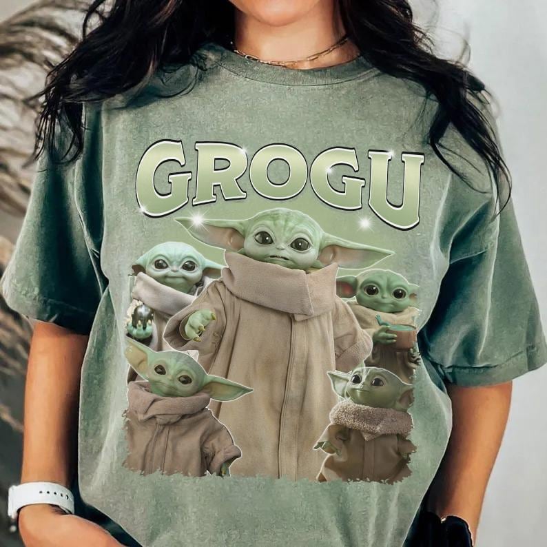 May include: Sage green t-shirt featuring the word "GROGU" in a light green, outlined font. The shirt displays multiple images of Grogu, a character from The Mandalorian, in various poses. The design is centered on the front of the shirt.
