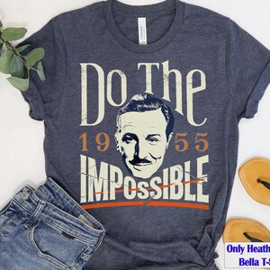 Pu&ograve; includere: T-shirt Bella blu navy melange con la scritta "Do the Impossible" e un ritratto di un uomo. L'anno "1955" &egrave; stampato sopra la parola "Impossible". La maglietta &egrave; abbinata a jeans blu e sandali.