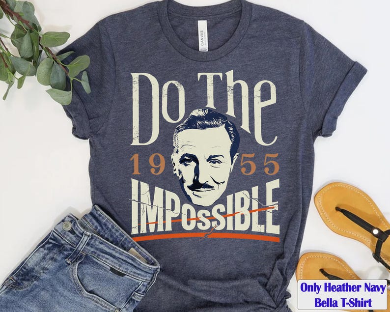 Pu&ograve; includere: T-shirt Bella blu navy melange con la scritta "Do the Impossible" e un ritratto di un uomo. L'anno "1955" &egrave; stampato sopra la parola "Impossible". La maglietta &egrave; abbinata a jeans blu e sandali.