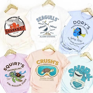 May include: Six short-sleeve t-shirts in various colors, each featuring a unique graphic print inspired by ocean life. Designs include a shark, a seagull, a blue fish, a sea turtle with snorkeling gear, a sea turtle in goggles, and a shark with text.