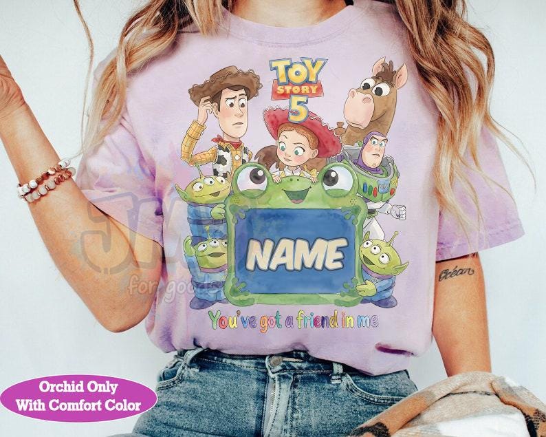 May include: A light purple t-shirt featuring a Toy Story 5 graphic with Woody, Jessie, Bullseye, Buzz Lightyear, and three aliens surrounding a green frog holding a blue sign that says NAME, with the text You've got a friend in me below.