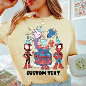 Op de afbeelding: Lichtgele t-shirt met een verjaardagstaart, Spider-Man-personages en ballonnen. De taart is versierd in rood, wit en blauw. De tekst "CUSTOM TEXT" staat onderaan.