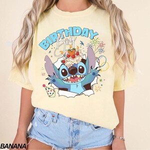 K&ouml;nnte beinhalten: Hellgelbes T-Shirt mit einem Cartoon-Charakter. Die blaue Figur mit gro&szlig;en Augen und einem breiten Grinsen bricht durch einen zerrissenen Papiereffekt und h&auml;lt einen Geburtstagskuchen. Der Text "BIRTHDAY Boy" steht &uuml;ber der Figur.