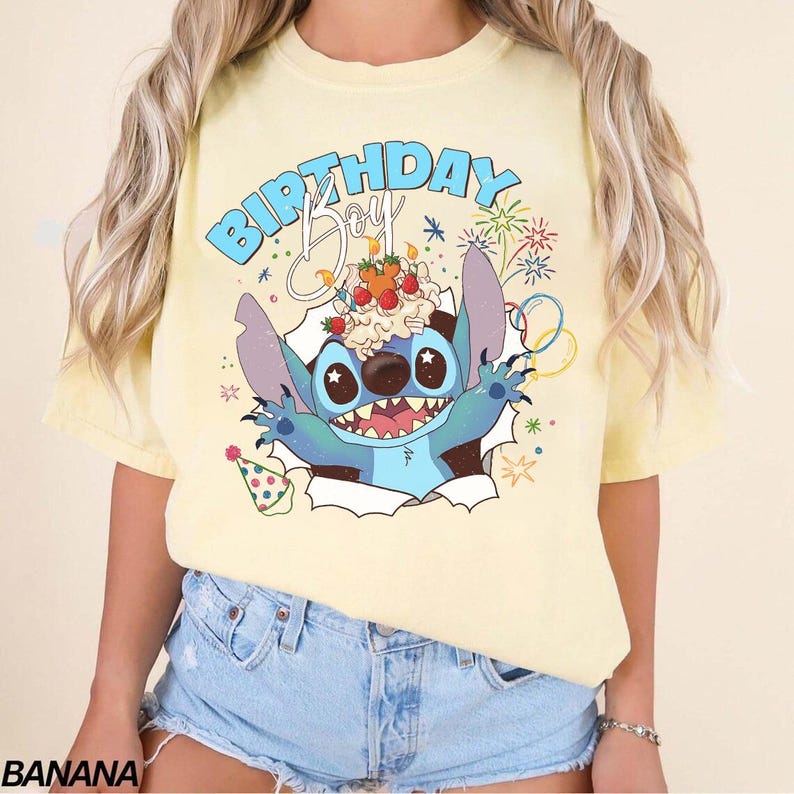 K&ouml;nnte beinhalten: Hellgelbes T-Shirt mit einem Cartoon-Charakter. Die blaue Figur mit gro&szlig;en Augen und einem breiten Grinsen bricht durch einen zerrissenen Papiereffekt und h&auml;lt einen Geburtstagskuchen. Der Text "BIRTHDAY Boy" steht &uuml;ber der Figur.
