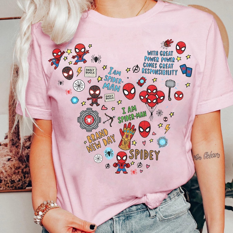 Puede incluir: Camiseta rosa claro con un dise&ntilde;o en forma de coraz&oacute;n de Spider-Man. El dise&ntilde;o incluye los textos "I AM SPIDER-MAN", "SPIDEY" y "BRAND NEW DAY", junto con estrellas, rayos y otros elementos de c&oacute;mic.