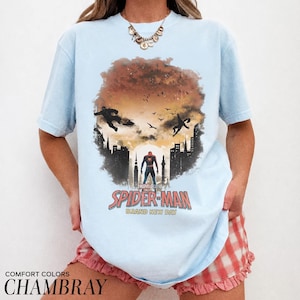 Pu&ograve; includere: Una t-shirt azzurra con una stampa grafica di Spider-Man in piedi davanti alla sagoma di una citt&agrave; su un cielo al tramonto. Il design include sagome di figure volanti, uccelli e la scritta Spider-Man Brand New Day in lettere rosse e bianche.