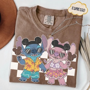 May include: Espresso-colored t-shirt featuring a cartoon graphic of two characters, one blue and one pink, holding ice cream. The blue character wears sunglasses and a Hawaiian shirt. The pink character wears heart-shaped sunglasses and a skirt. The shirt has a Comfort Colors tag.