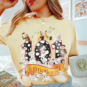 May include: Yellow t-shirt featuring a graphic of 101 Dalmatians. The design includes the number 101 with Dalmatian spots, various Dalmatian characters, and the word "Dalmatians" on a banner. The shirt has a crew neck.
