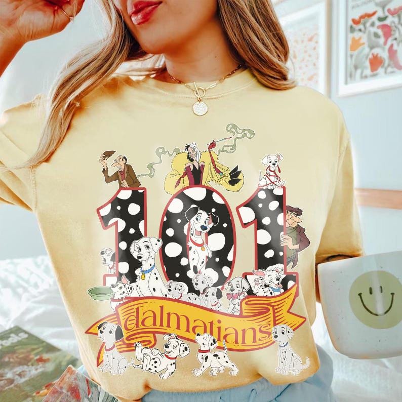 May include: Yellow t-shirt featuring a graphic of 101 Dalmatians. The design includes the number 101 with Dalmatian spots, various Dalmatian characters, and the word "Dalmatians" on a banner. The shirt has a crew neck.