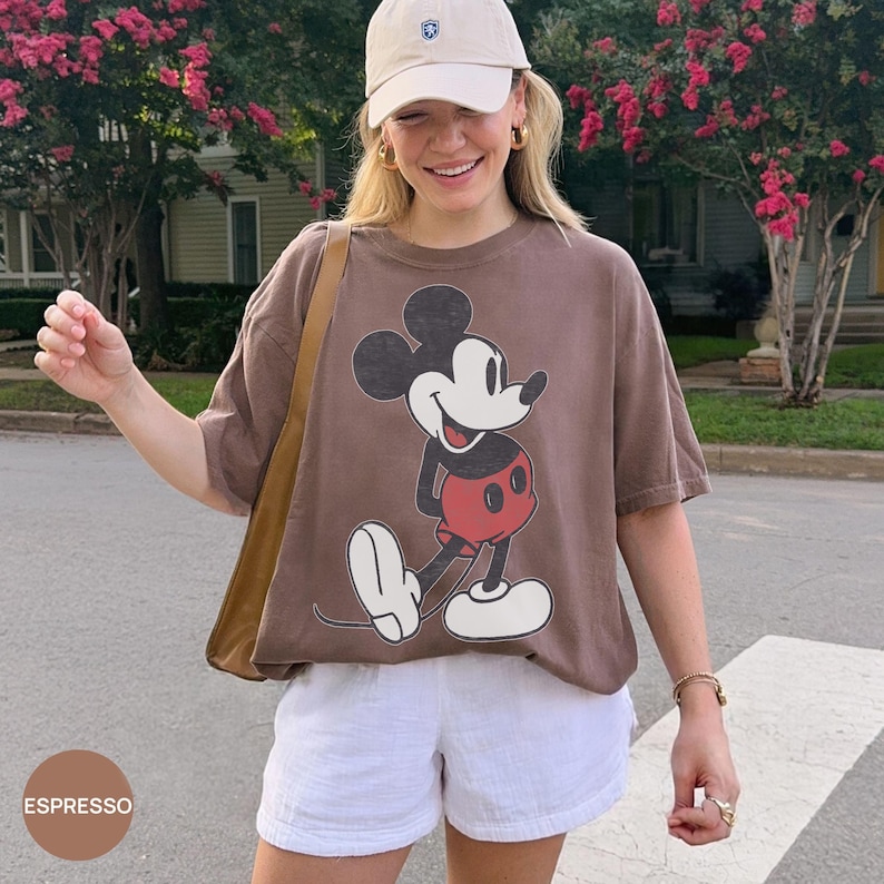 Peut inclure: Un t-shirt marron avec un dessin de Mickey Mouse en noir, rouge et blanc. Le t-shirt est port&eacute; avec un short blanc et une casquette de baseball beige. Le mot "ESPRESSO" est dans un cercle en bas &agrave; gauche.