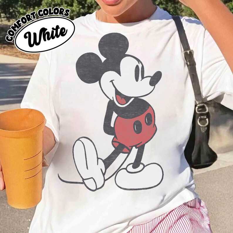 Peut inclure: T-shirt blanc avec un dessin de Mickey Mouse en noir, blanc et rouge. Le t-shirt porte les mots "COMFORT COLORS" et "White". Le t-shirt est un v&ecirc;tement d&eacute;contract&eacute;.