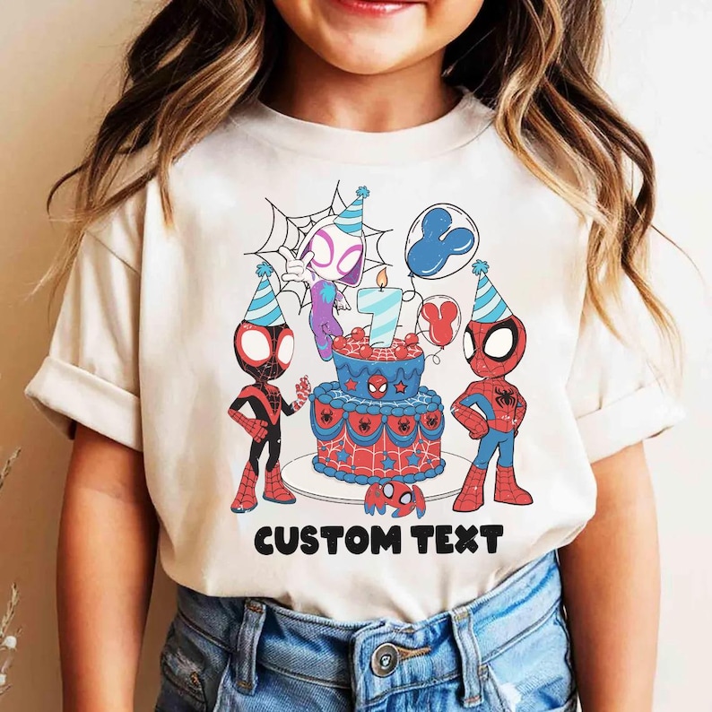 Op de afbeelding: Een beige t-shirt met een verjaardagstaartontwerp met het nummer 7, Spider-Man-personages en ballonnen. De woorden "CUSTOM TEXT" staan eronder in het zwart gedrukt. Het t-shirt wordt door een kind gedragen.