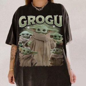 May include: Black t-shirt featuring the word "GROGU" in green letters above a graphic of Grogu from The Mandalorian. The graphic shows Grogu in various poses, wearing a tan cloak.